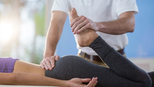 A woman laying face down on a treatment table while a physical therapist examines her leg